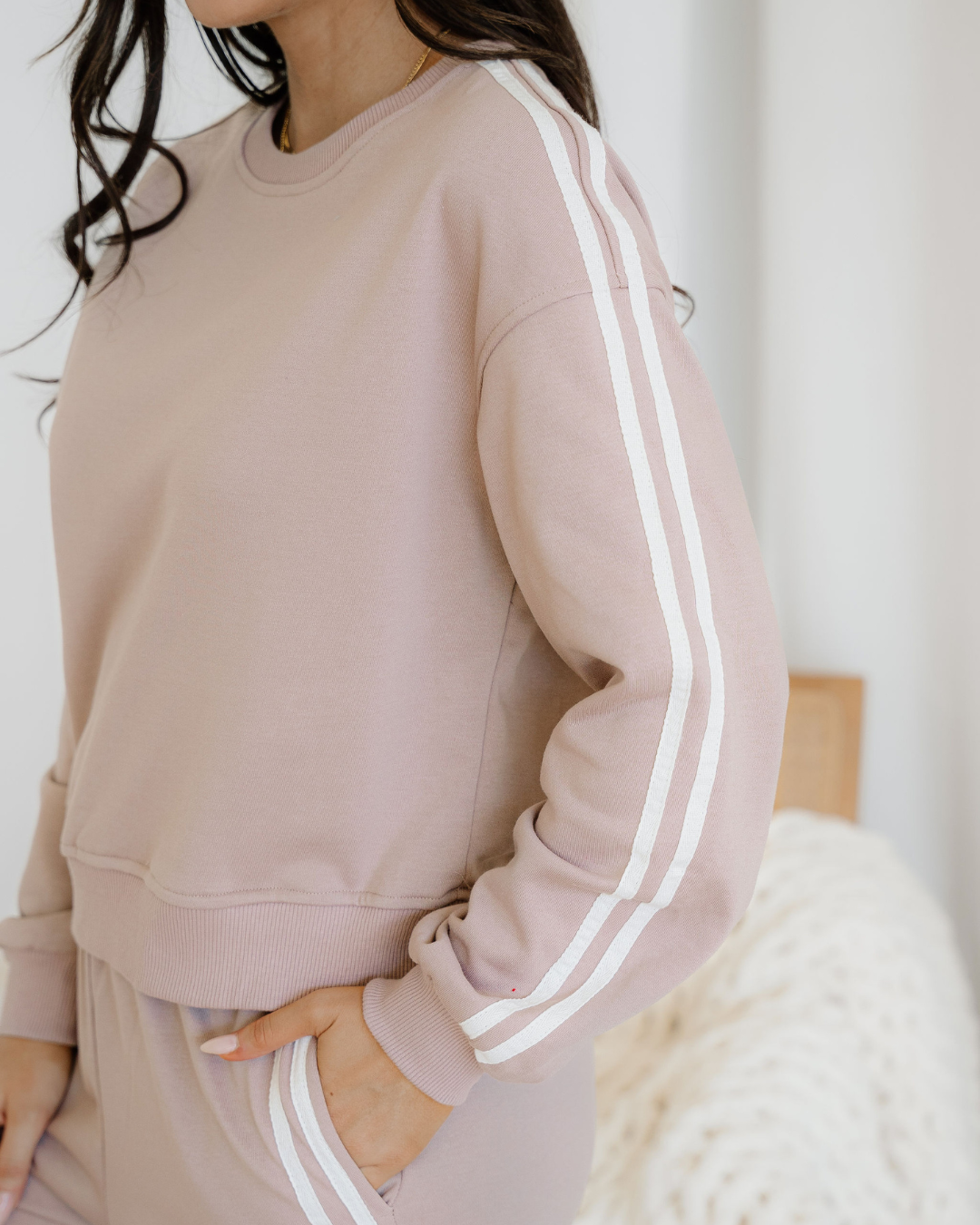 Person wearing a pink sweatshirt with white stripes, sitting on a white surface.