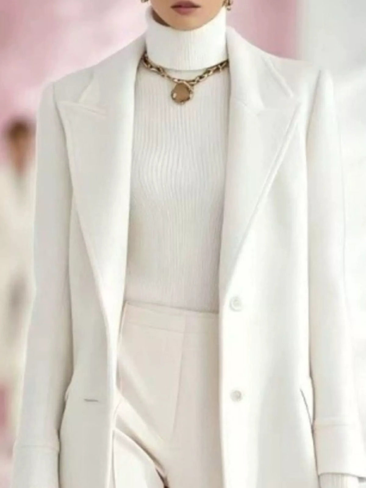 Model wearing a white longline coat with a lapel collar and button front over a white turtleneck and white trousers.