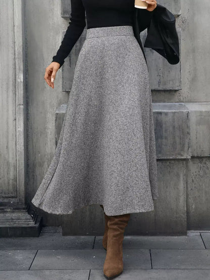 Person wearing a gray skirt and brown boots against a concrete wall.