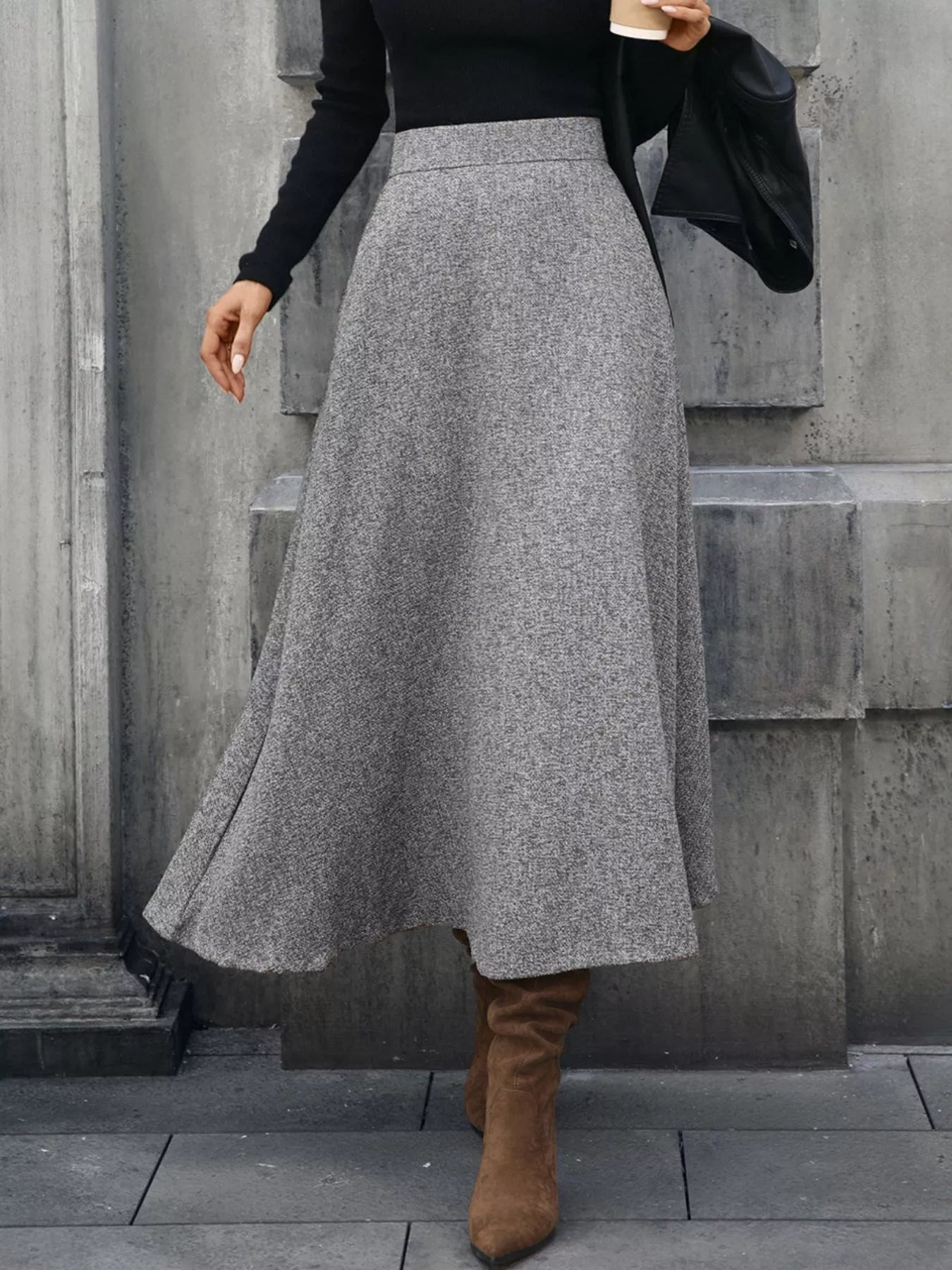 Person wearing a gray skirt and brown boots against a concrete wall.