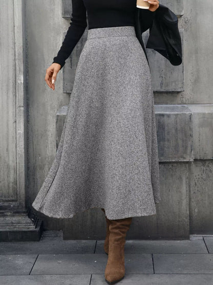 Person wearing a gray skirt and brown boots against a concrete wall.