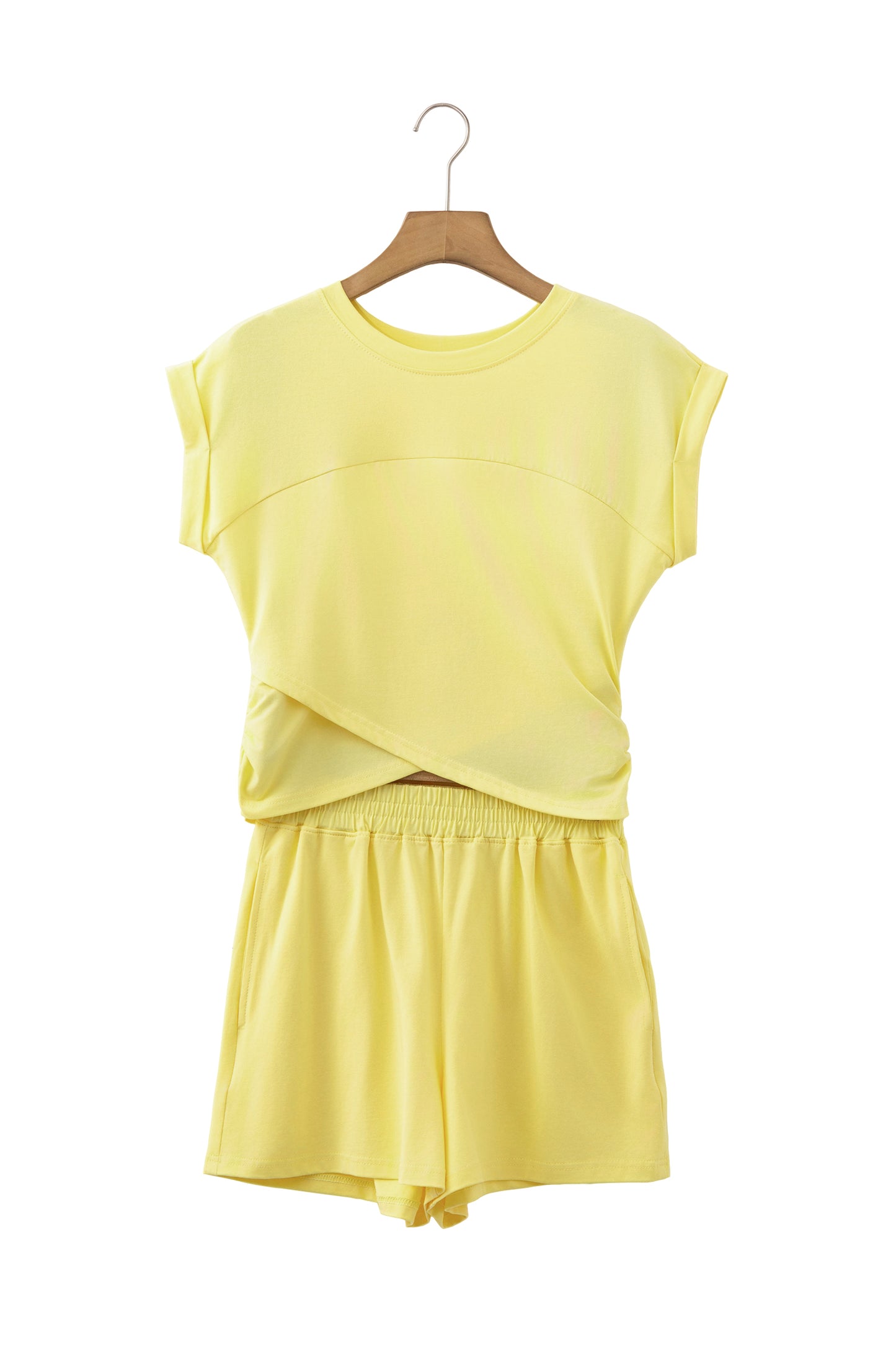 A two-piece women's lounge set in pale yellow, featuring a short-sleeve crewneck top with a crossover front detail and matching shorts, displayed on a wooden hanger against a white background.