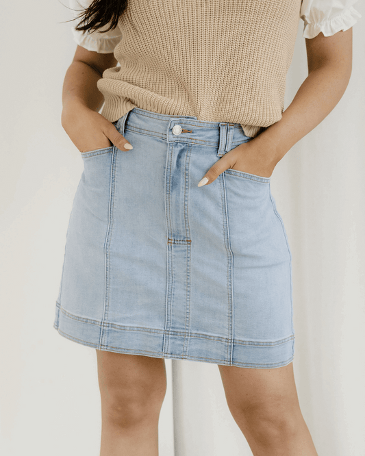 Person wearing a light blue denim skirt with a neutral background