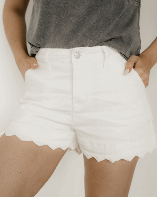 Woman wearing white denim scalloped hem shorts.