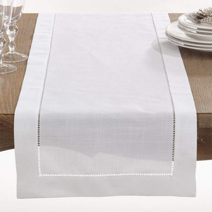 White table runner on a wooden table with plates and glasses.