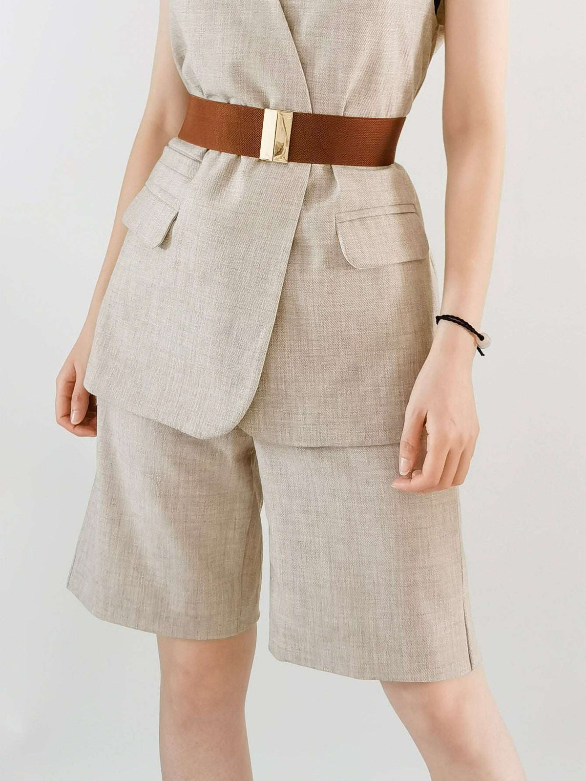 Person wearing a beige suit with a brown belt on a plain background