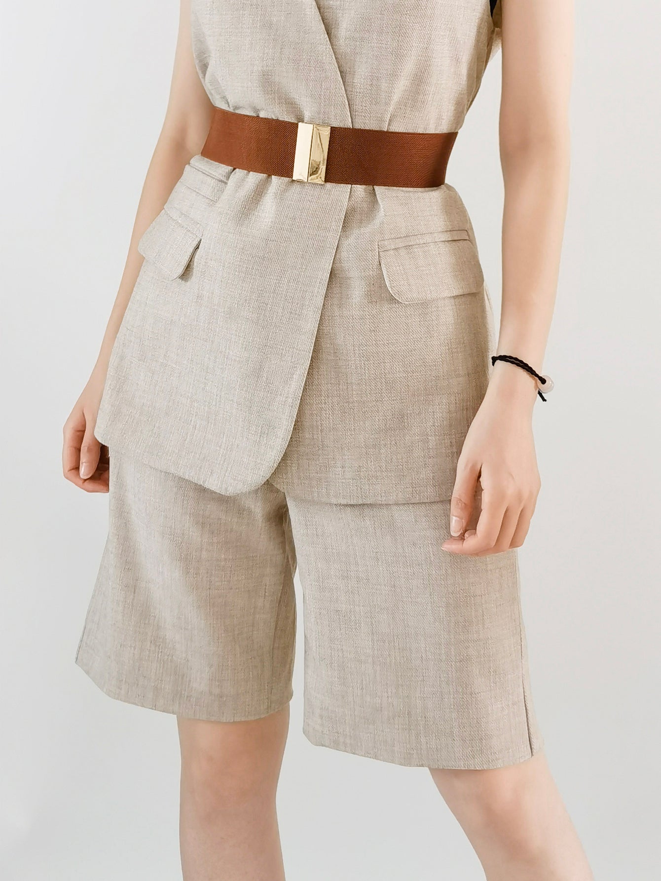 Person wearing a beige suit with a brown belt on a plain background