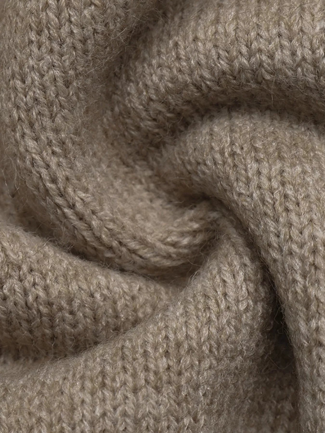 A close-up of a soft, knitted fabric in a warm taupe-beige color, showing the detailed knit texture and draped folds.