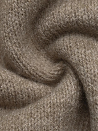 A close-up of a soft, knitted fabric in a warm taupe-beige color, showing the detailed knit texture and draped folds.