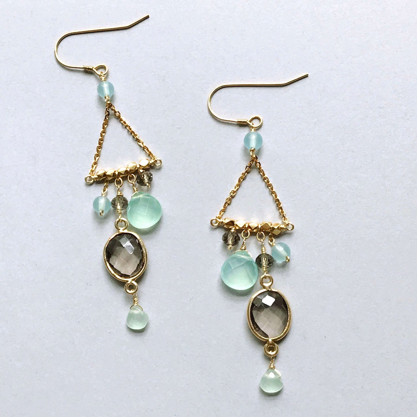 Gold earrings with green gemstones on a light gray background