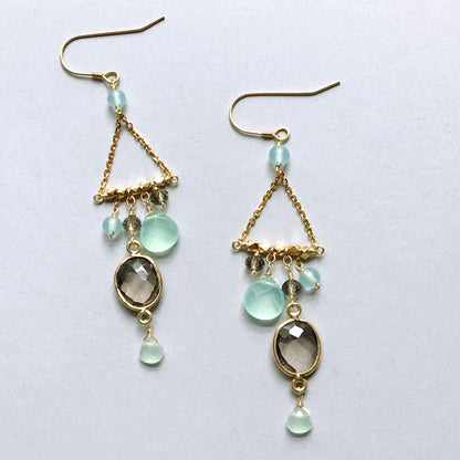 Gold earrings with green gemstones on a light gray background