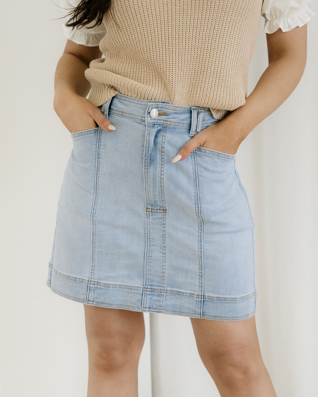 Person wearing a light blue denim skirt with a neutral background