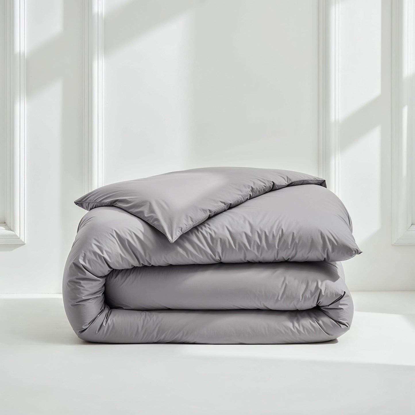 Folded gray comforter with pillows on a white surface