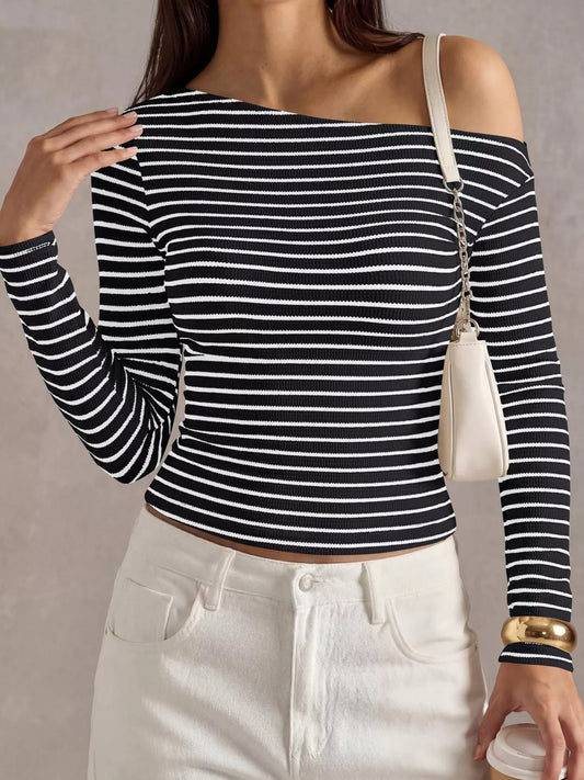 A woman wearing a black and white horizontally striped off-the-shoulder long-sleeve crop top, paired with white pants and a small cream shoulder bag.