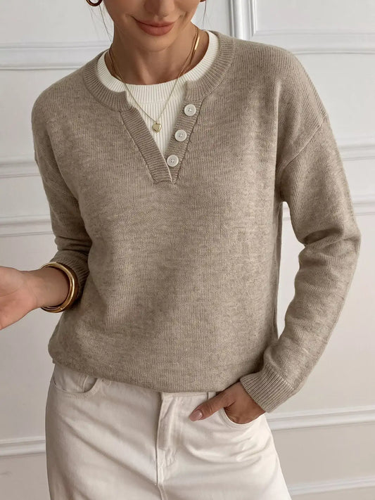 A woman wearing a taupe-beige ribbed knit henley sweater over a cream ribbed top and cream pants, accessorized with gold jewelry.