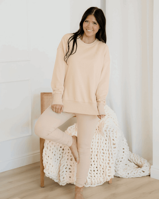 Woman in a beige outfit sitting on a chair with a white textured blanket.