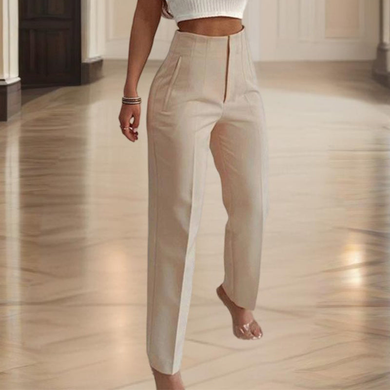 Person wearing beige high-waisted pants in a room with wooden flooring.