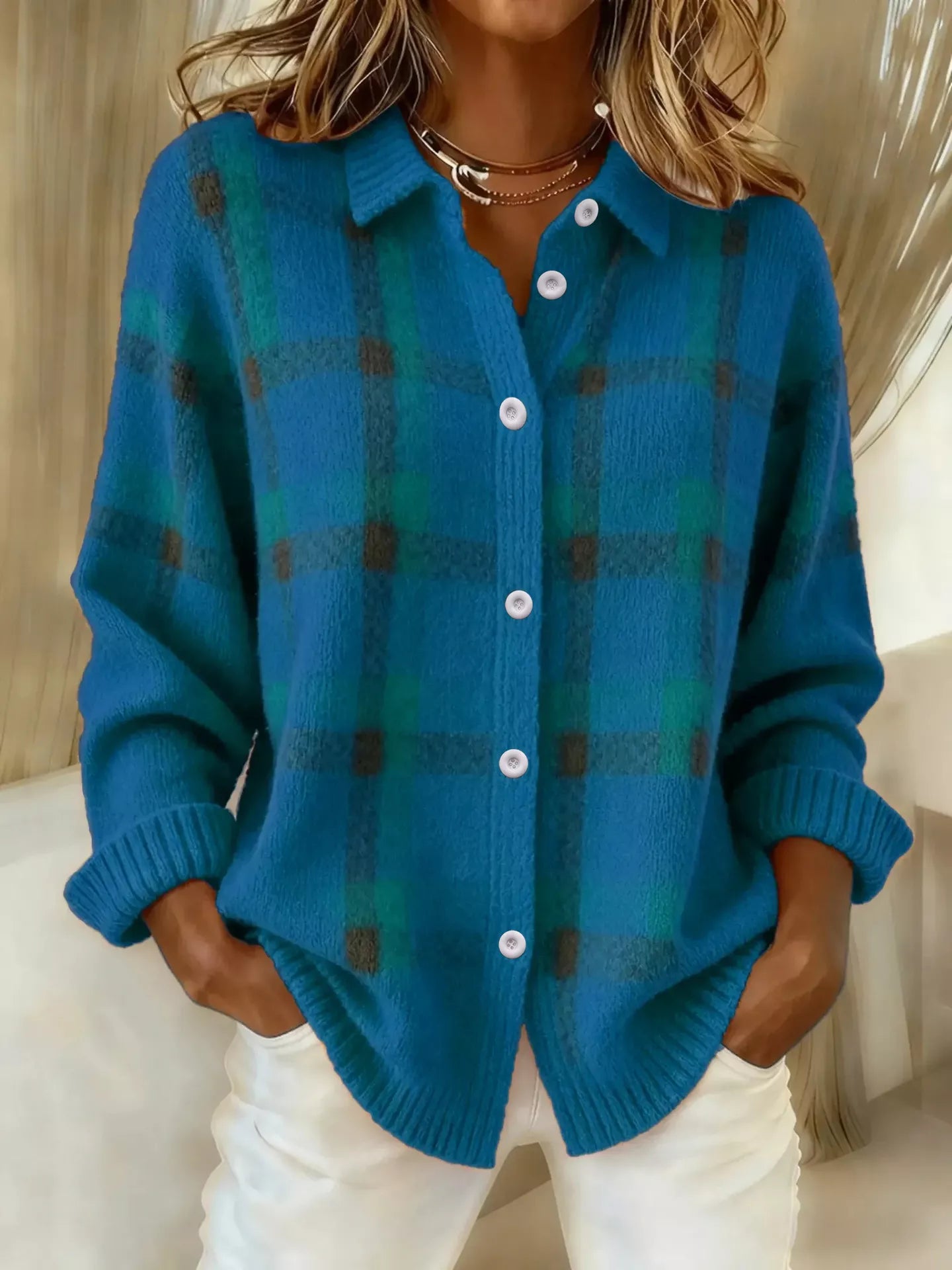 Person wearing a blue plaid cardigan with white pants indoors.