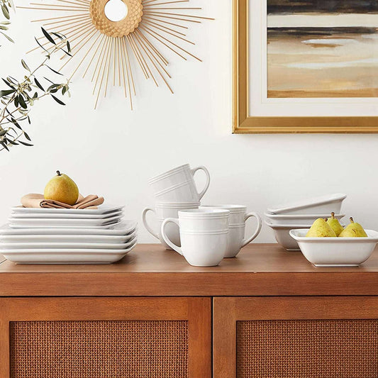 White stoneware dinnerware set on a wooden cabinet with decorative elements.