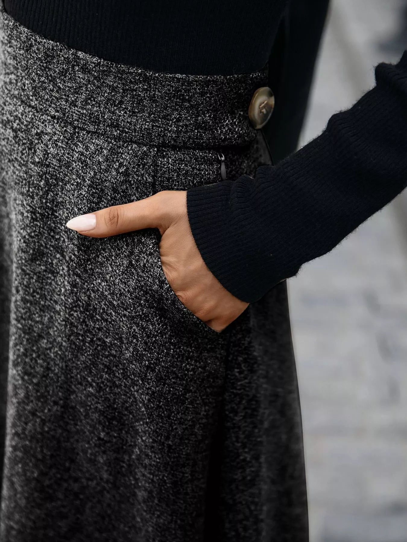 Person wearing a black sweater and gray textured skirt with a blurred background