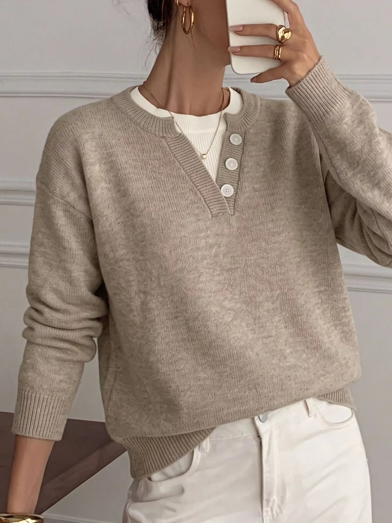 A person wearing a light taupe knit henley sweater over a white undershirt and white pants, shown in a mirror selfie style.