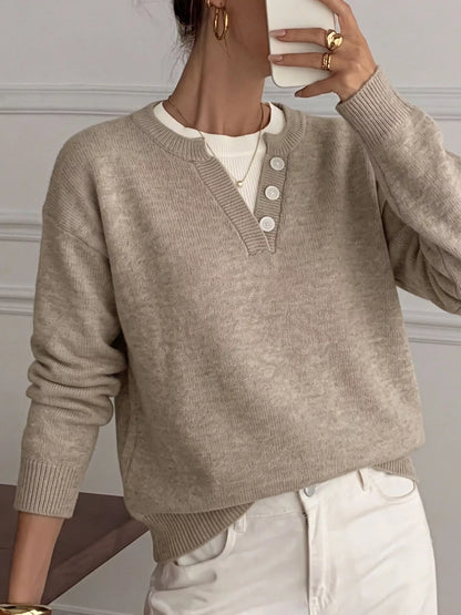 A person wearing a light taupe knit henley sweater over a white undershirt and white pants, shown in a mirror selfie style.