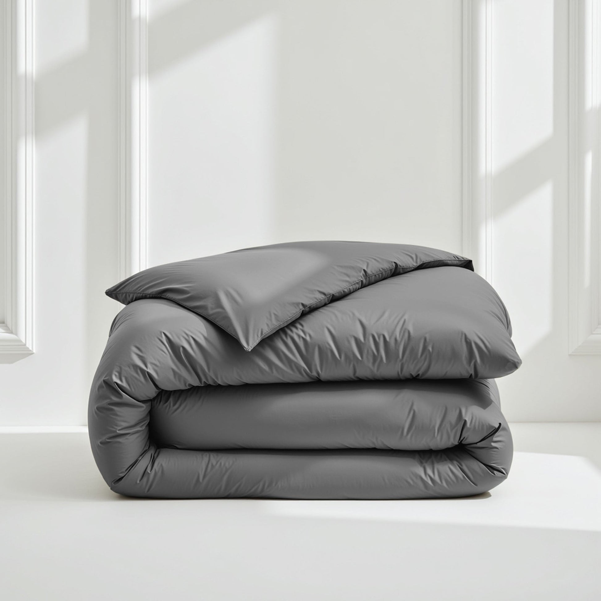 Folded gray comforter on a white surface with a light gray wall background