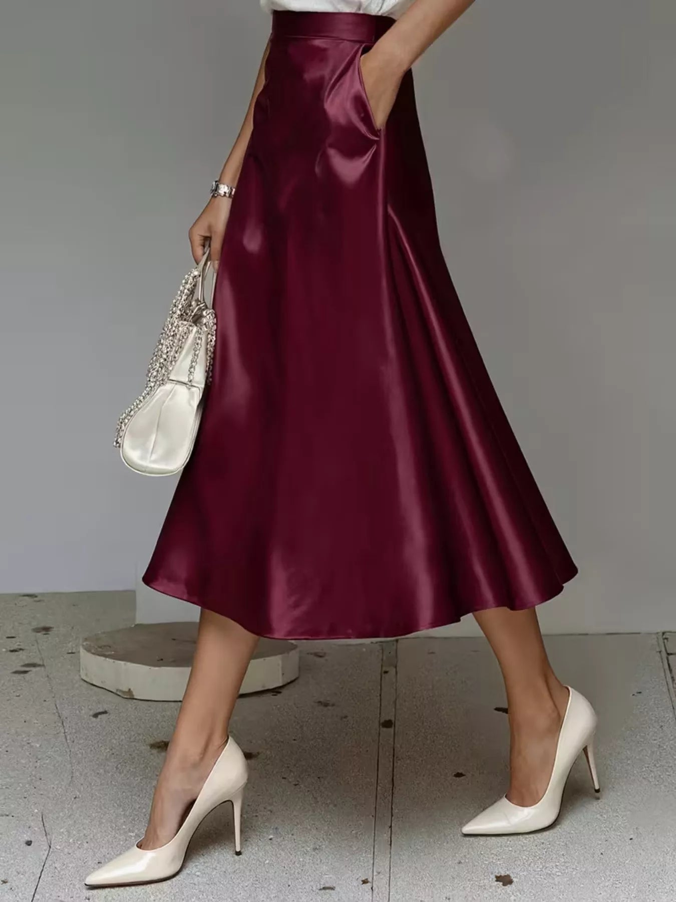 Person wearing a burgundy satin skirt with white high-heeled shoes on a neutral background