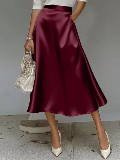 Person wearing a burgundy satin skirt with a plain background