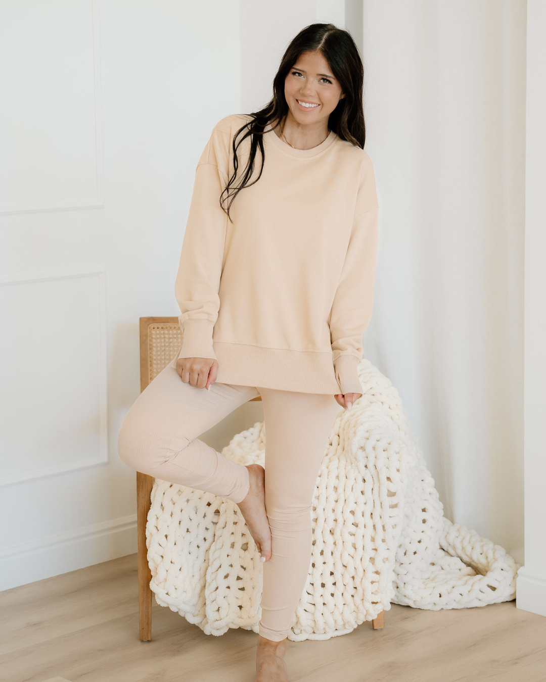 Woman in a beige outfit sitting on a chair with a white textured blanket.