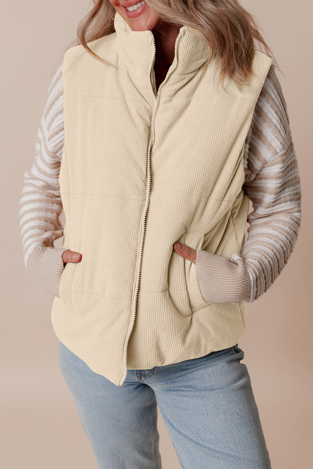Woman wearing a beige puffer vest over a striped sweater with a neutral background