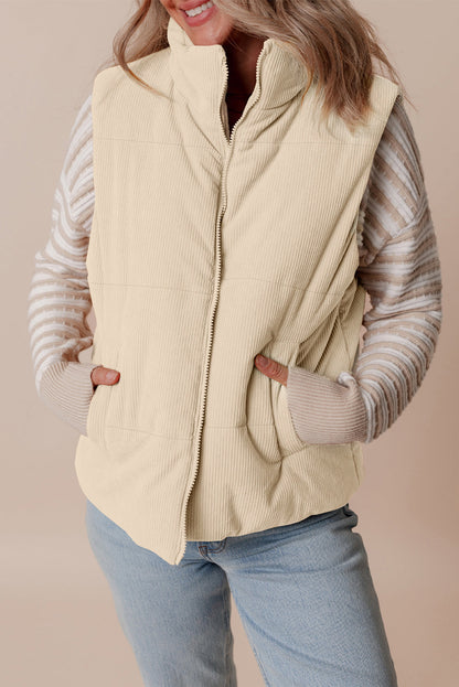 Woman wearing a beige puffer vest over a striped sweater with a neutral background