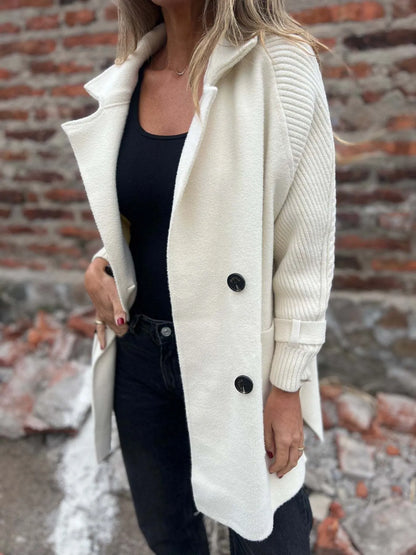 Model wearing a white double-breasted coat with cable-knit sleeves, buckled cuffs, wide lapels and front pockets.