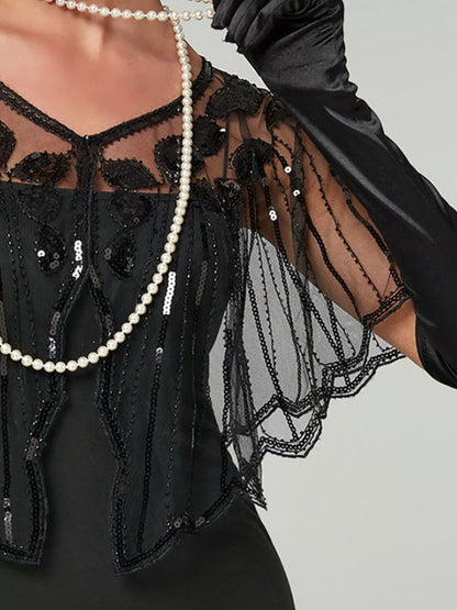 Model wearing a black sheer sequin capelet with a shallow V-neck, floral embellishments and scalloped edges over a black dress