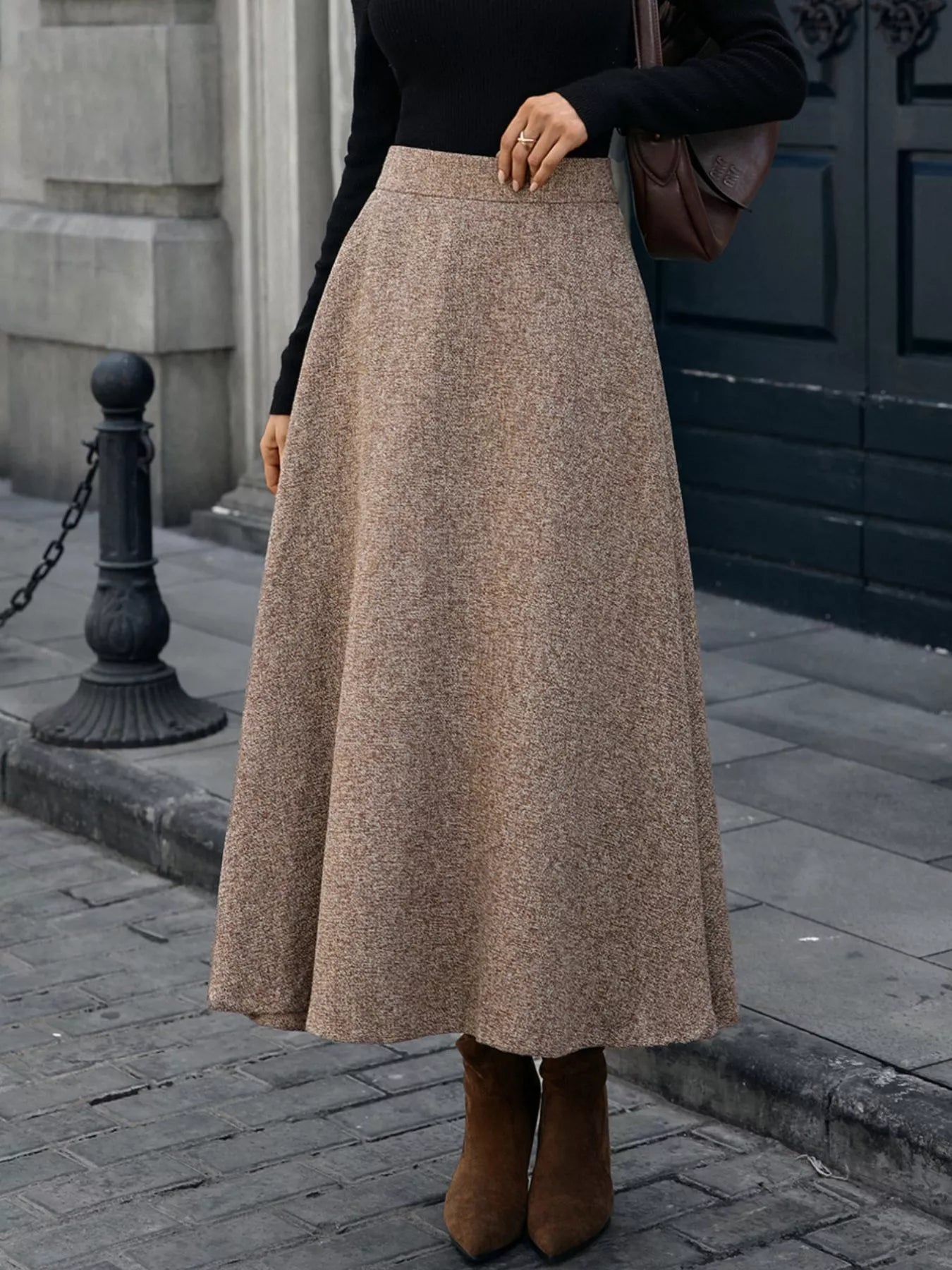 Person wearing a long beige skirt and brown boots on a city street.