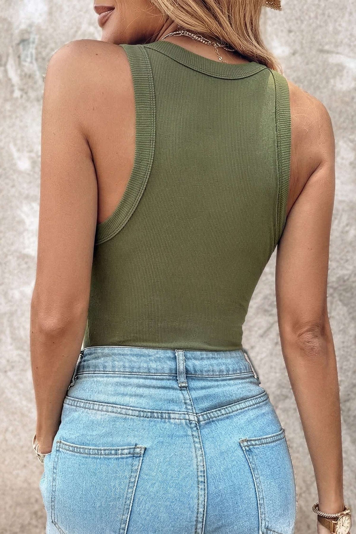 Rear view of a person wearing an olive green ribbed fabric tank top tucked into light wash denim jeans.