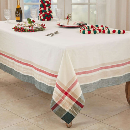 A holiday-themed tablecloth set displayed on a dining table, featuring a white tablecloth with red and beige stripes and a green plaid pattern, along with matching napkins, a festive mini tree, and holiday tableware.