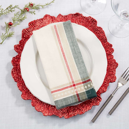 A folded holiday-themed napkin with cream, red, gray, and green plaid and stripe patterns, styled on a white plate over a red scalloped charger plate on a white tablecloth.