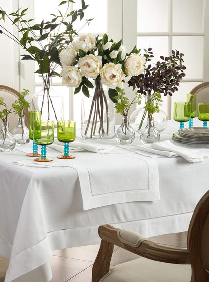 Elegant table setting with white tablecloth, green glasses, and floral arrangements.