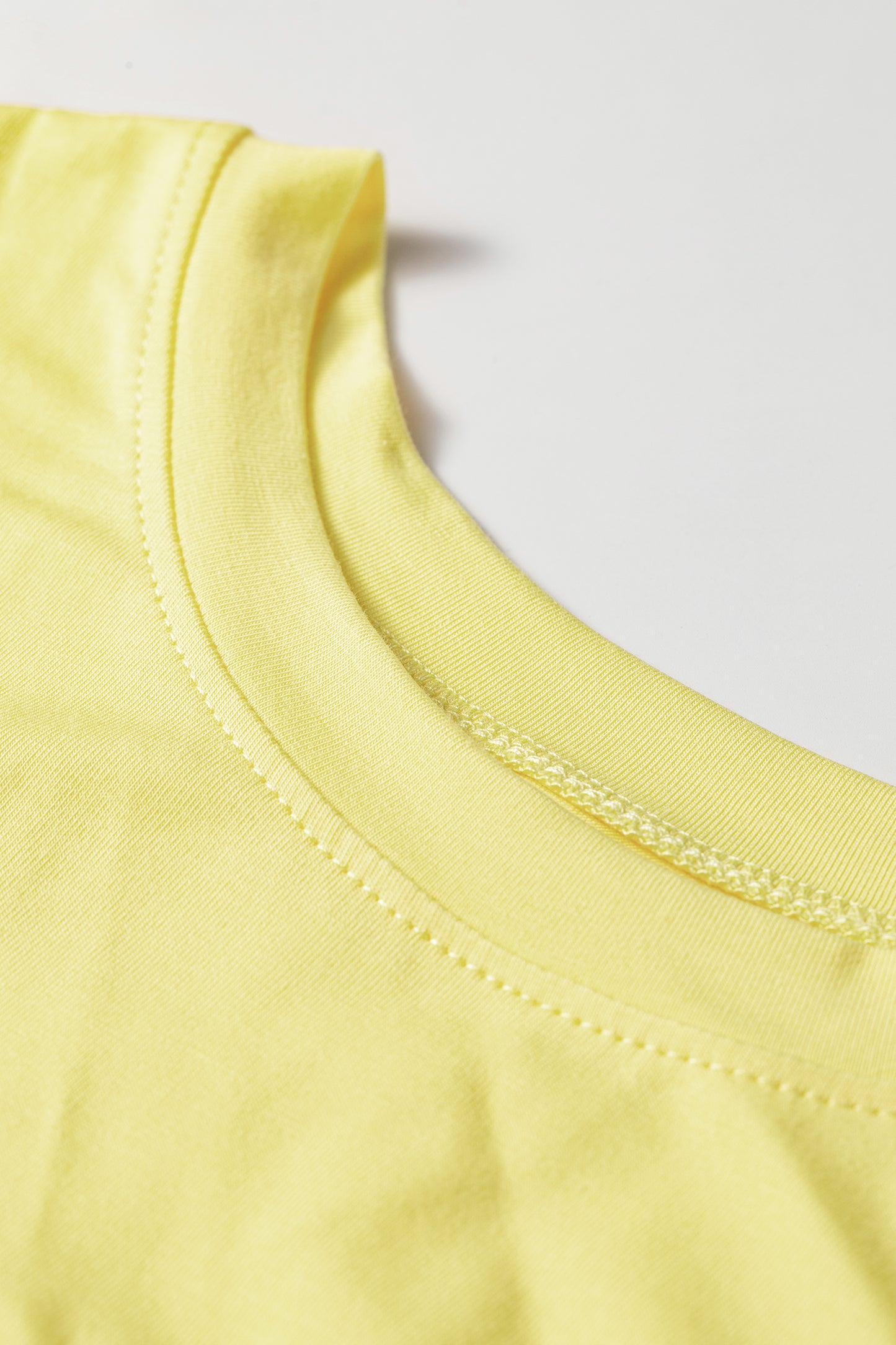 Close-up of a light yellow crew-neck t-shirt showing the ribbed collar and stitching details against a plain light gray background.
