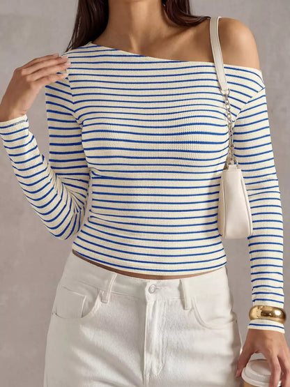 A woman wearing a blue and white horizontally striped off-the-shoulder long-sleeve ribbed top, paired with white pants and a small white shoulder bag.