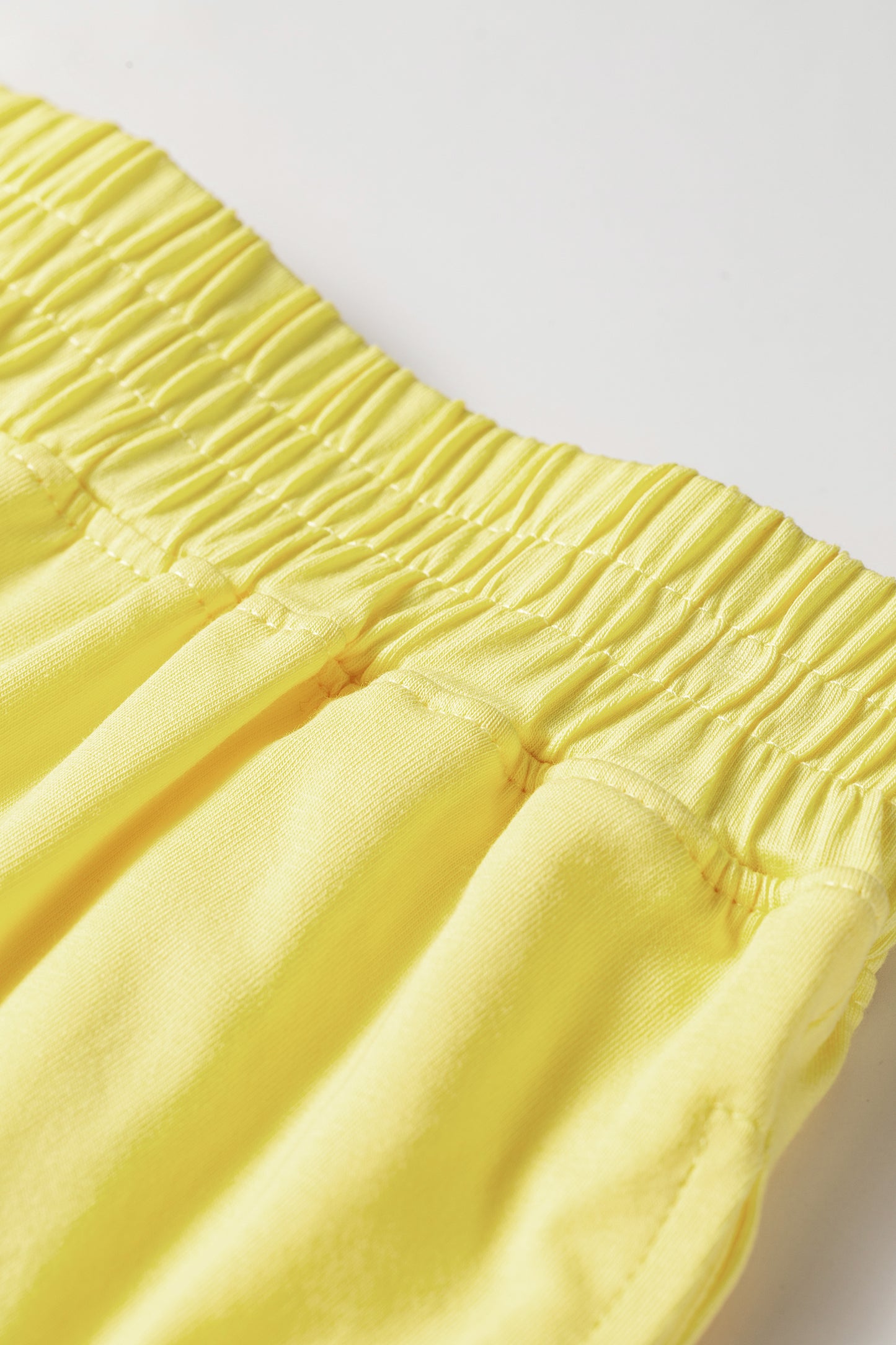 Close-up of a bright yellow garment with an elasticized gathered waistband, photographed against a plain light background.