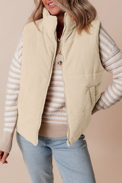 Person wearing a beige puffer vest over a striped sweater with a beige background