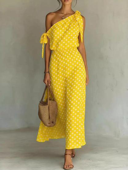 Woman wearing a yellow polka dot dress holding a woven bag against a plain background