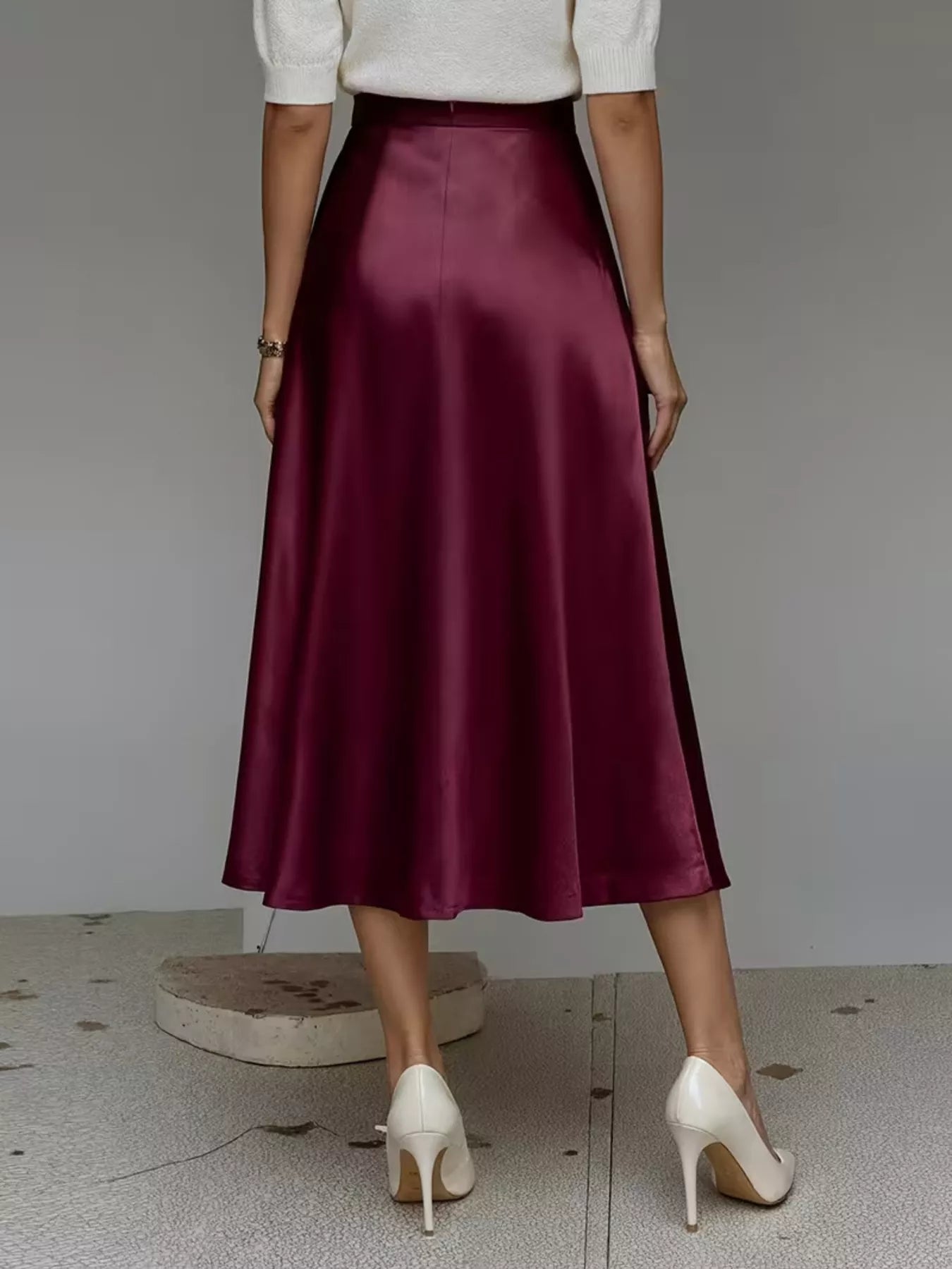 Person wearing a burgundy satin skirt with a plain background