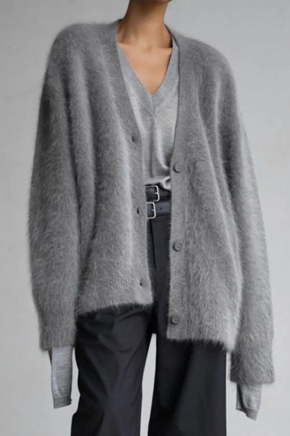 Person wearing a gray cardigan over a light gray shirt with dark pants on a plain background