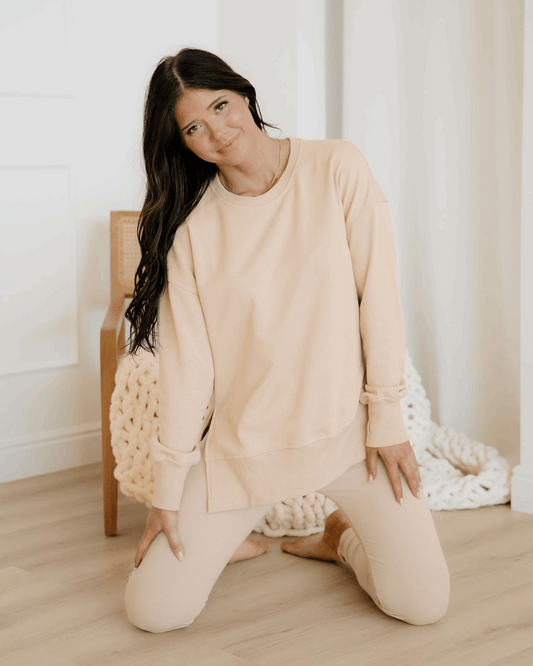 Woman in beige outfit sitting on the floor with a white background