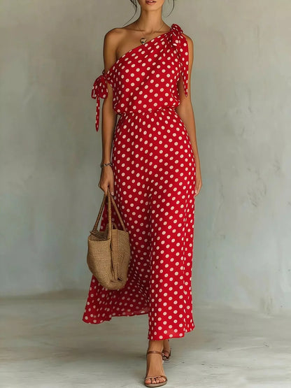 Woman wearing a red polka dot dress holding a woven bag against a plain background