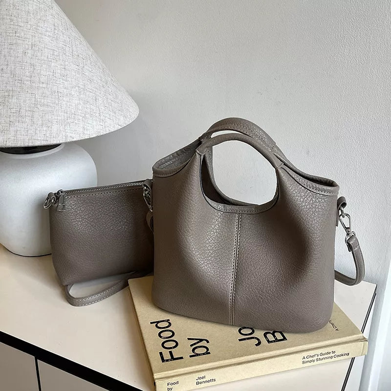 Gray handbag and wallet on a stack of books with a lamp in the background