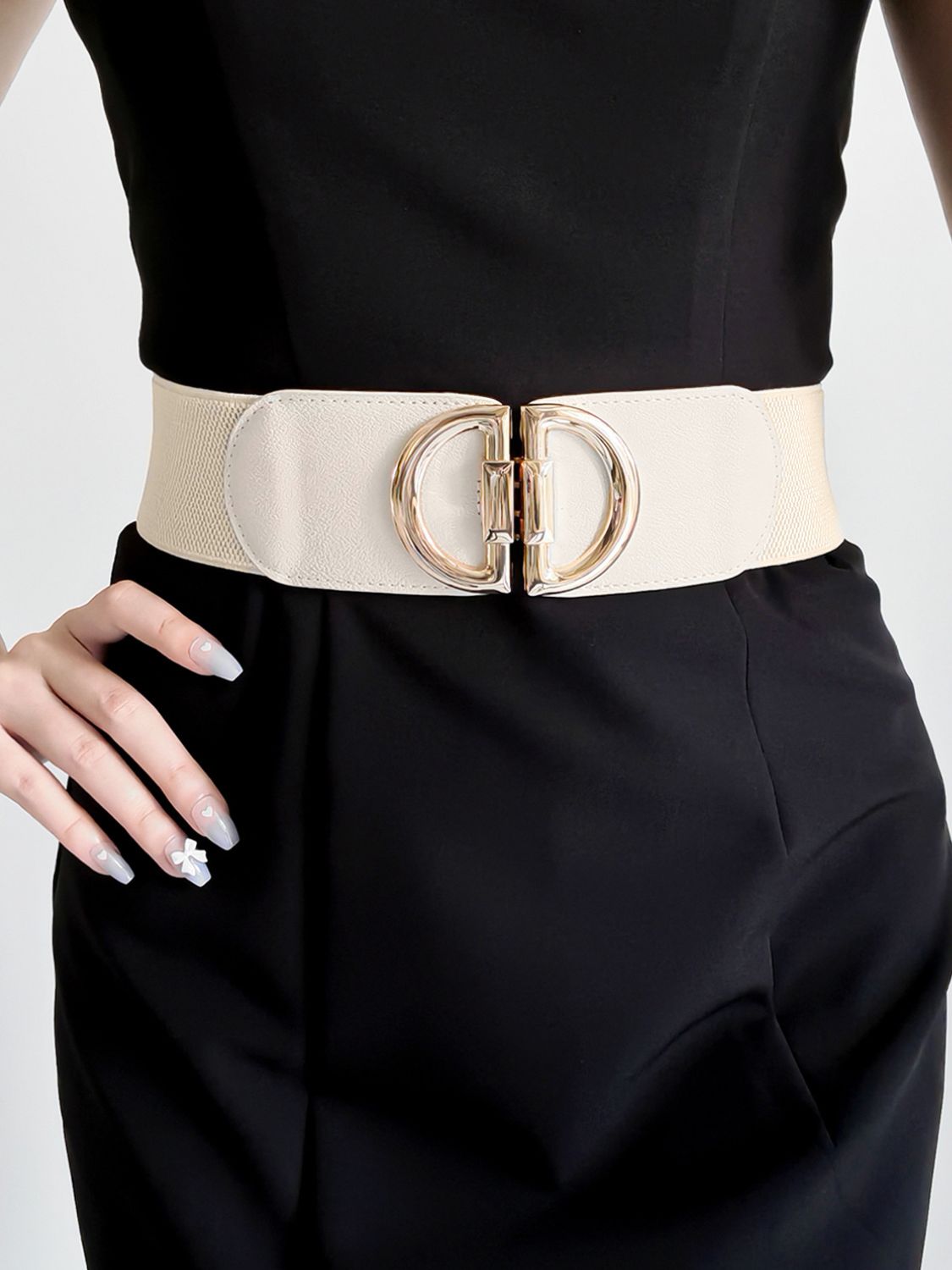 Person wearing a black outfit with a beige belt featuring a gold buckle on a white background